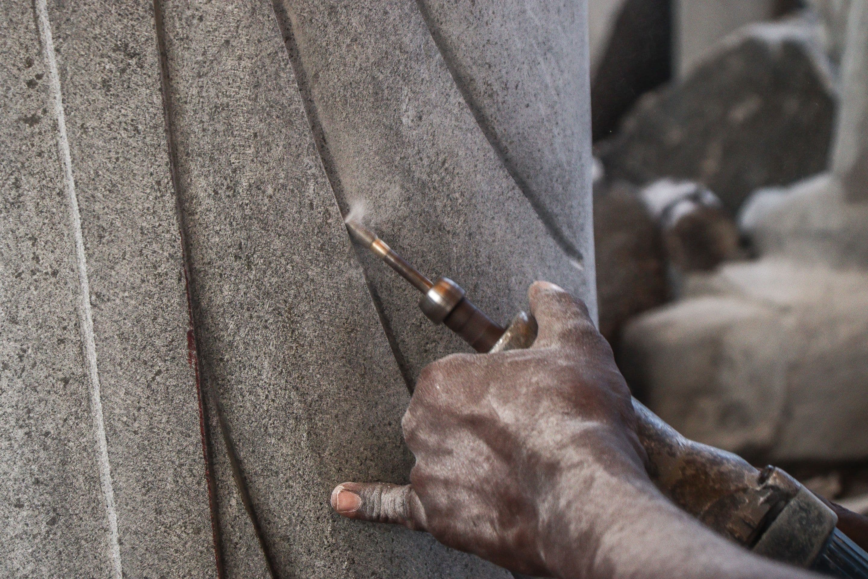 A stonemason's dust-covered hand guiding a chisel to carve a stone column